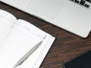 Open planner with a pen and laptop on a wooden desk, ready for organization.