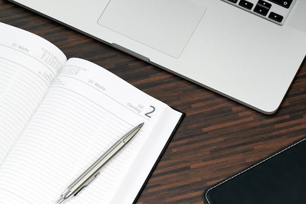 Open planner with a pen and laptop on a wooden desk, ready for organization.